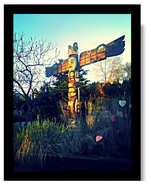 A garden with a colourful totem pole that has large wings extending to each side